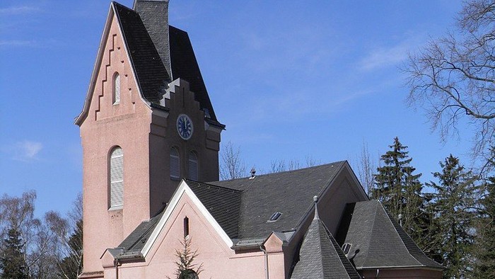 Kirchengebäude mit hohem Turm und Uhr, umgeben von Bäumen
