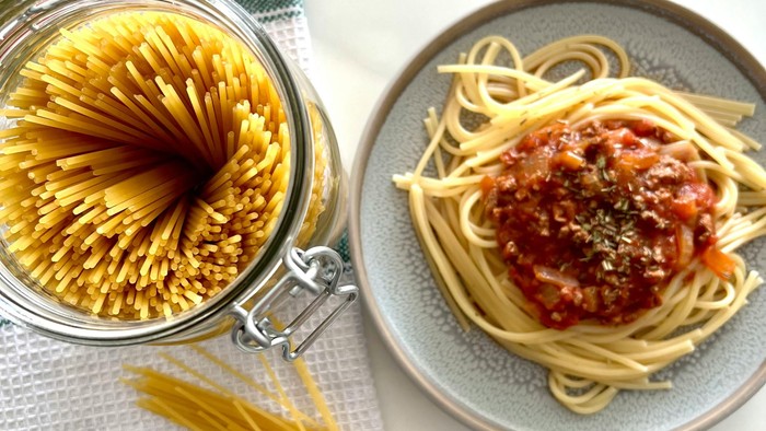 Frisk spaghetti med tomatsauce serveret på en tallerken ved siden af ubrygget pasta i en krukke.