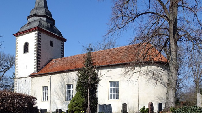 Weiße Kirche mit hohem Turm und rotem Dach unter blauem Himmel