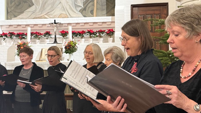 En gruppe kvinder, der synger sammen i en udsmykket kirke under en kormusikopførelse.