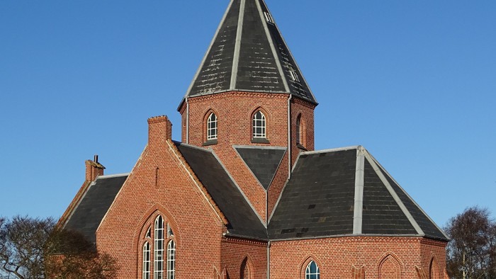 Røde murstenskirke med spiret og vindrosen.
