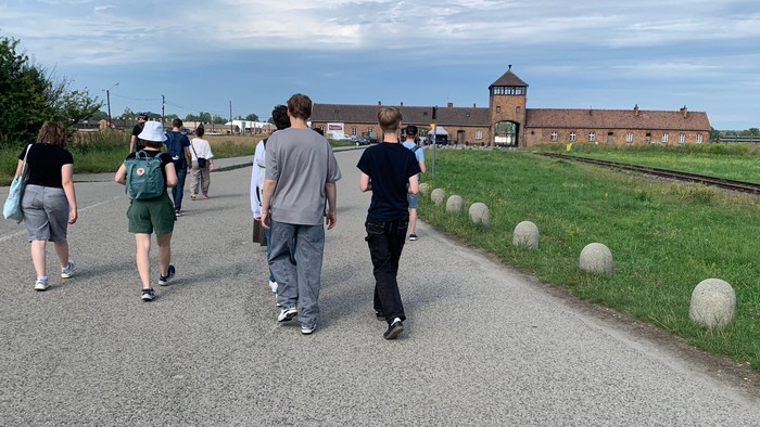 Eine Gruppe geht einen gepflasterten Weg entlang, in der Nähe eines historischen Backsteingebäudes und von Bahngleisen.