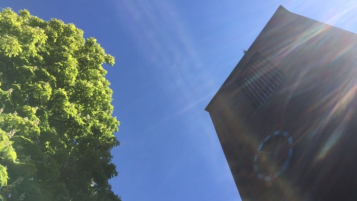 Der Kirchturm vor dem Maihimmel mit Kastanienbaum in voller Blüte.