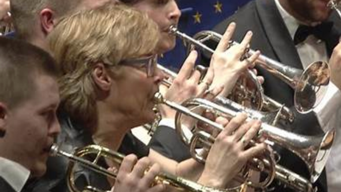 En gruppe musikere, der spiller messingblæsere i en formel koncertsammenhæng.