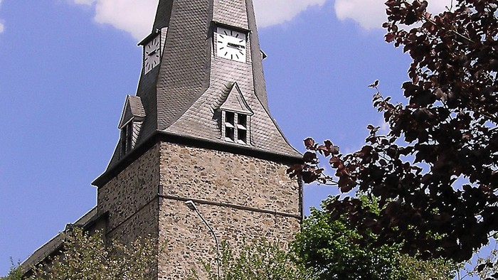 Ein hoher Kirchturm ragt in den klaren blauen Himmel.