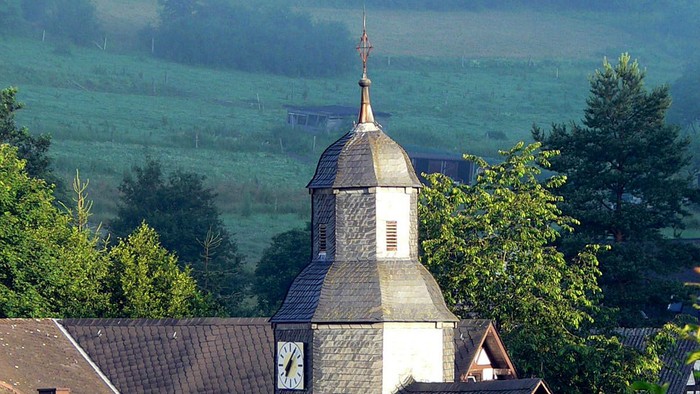 Dorfkirche mit grünem Hügel im Hintergrund