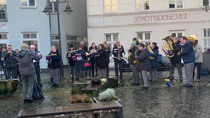 Eine Gruppe von Menschen spielt Musik auf einer Kopfsteinpflasterstraße vor einem Gebäude.