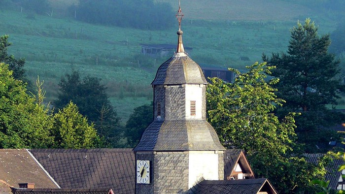 Dorfkirche mit grünem Hügel im Hintergrund