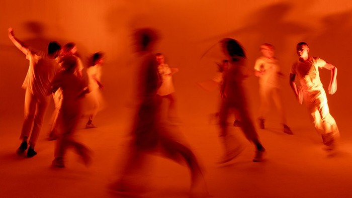 Personen bewegen sich in Raum. Alles in orange mit Bewegungsschärfe.