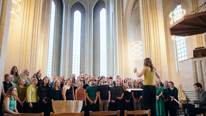 Et stort kor optræder i en stor katedral under en dirigents ledelse under en koncert.