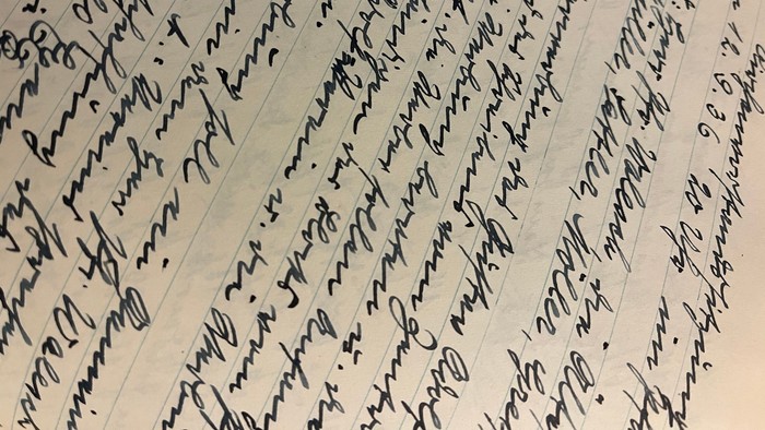 Dichte handschriftliche Schriftzüge, die in einem kunstvollen, fließenden Stil ein liniertes Papier bedecken.