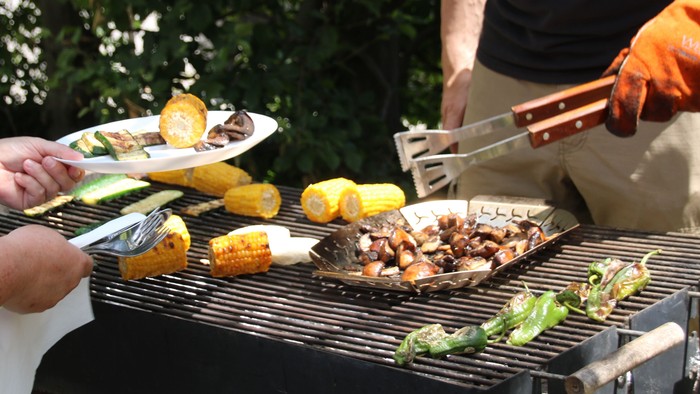 Zwei Personen grillen im Freien, verschiedene Lebensmittel auf dem Grill