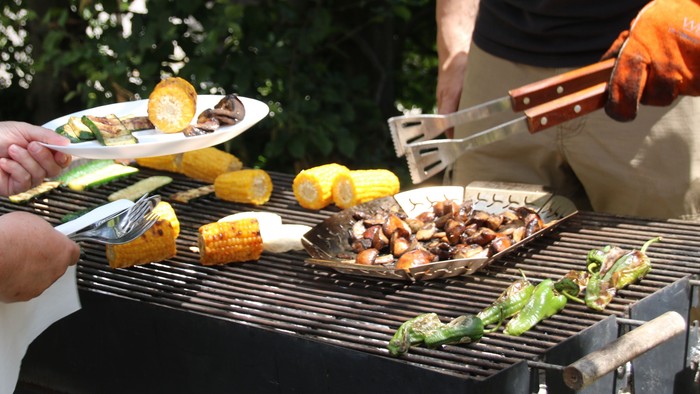 Zwei Personen grillen im Freien, verschiedene Lebensmittel auf dem Grill