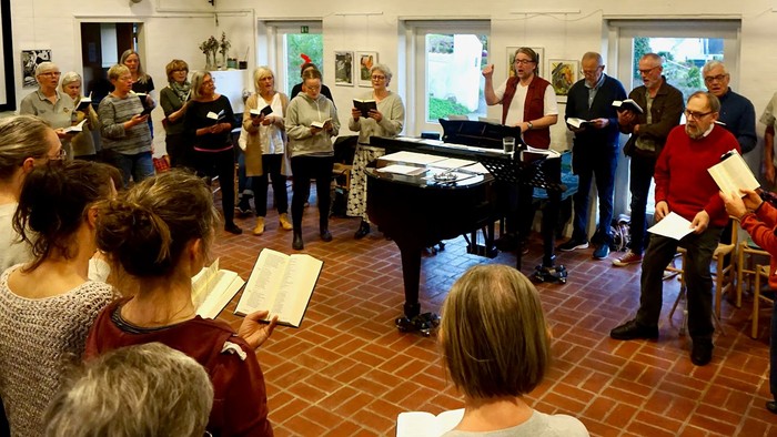 En gruppe mennesker, der synger sammen i et lokale med en pianist, der akkompagnerer dem.