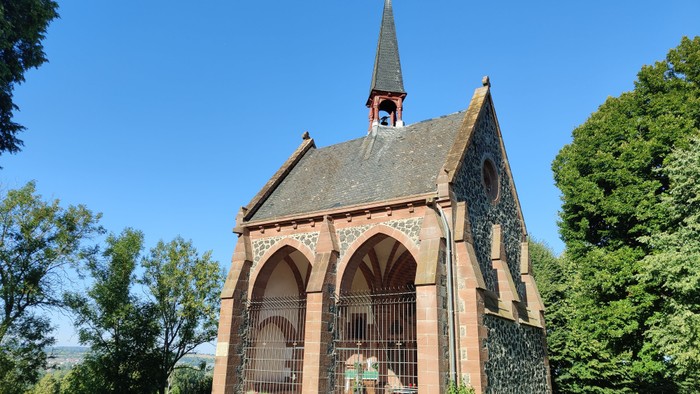 Idyllische Kapelle mit gewölbtem Eingang steht in einem ruhigen, gepflegten Friedhof unter klarem blauem Himmel.