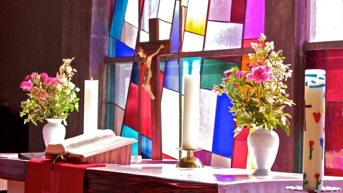 Buntes Kirchenfenster mit Kreuz, Blumen und Kerzen