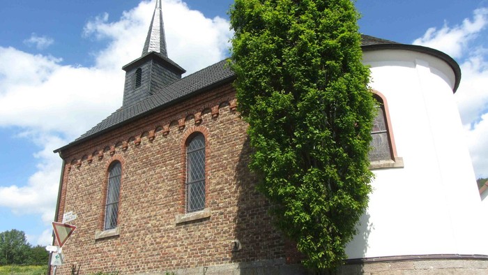 Ein Ziegelgebäude mit spitzem Dach und einem weißen Anbau neben einem hohen Baum