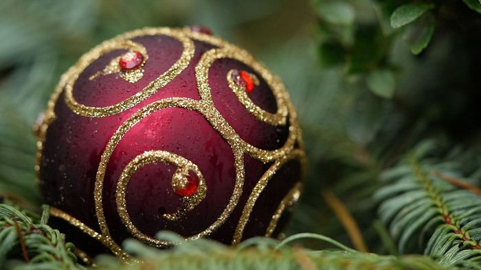 En rød og guld pyntet julekugle på en grøn kæmpe.