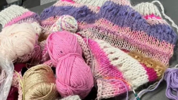 En samling strå og ufuldendte strømper i rosa, lilla og hvidt.