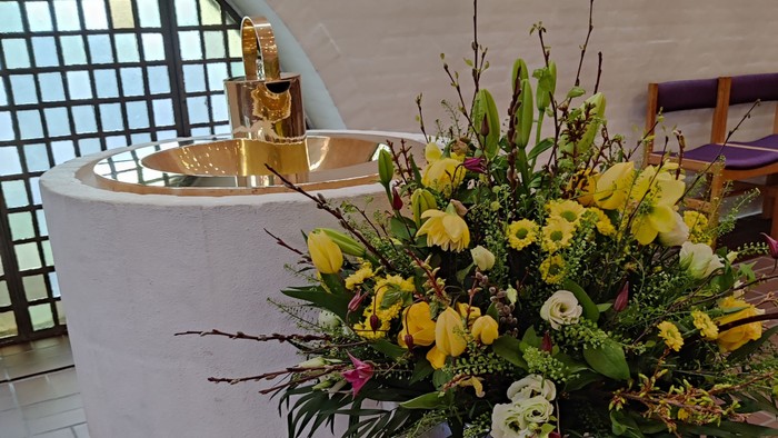 En stor blomsterarrangement med gule og hvide blomster står på en stativ foran en fontæne.
