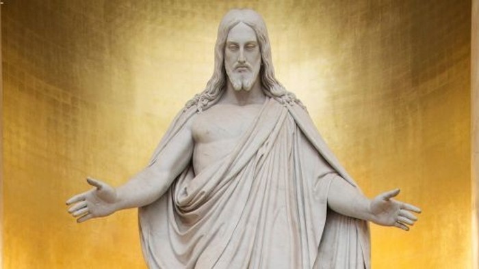 Statuen af Jesus med udbredede arme foran guldgul væg.