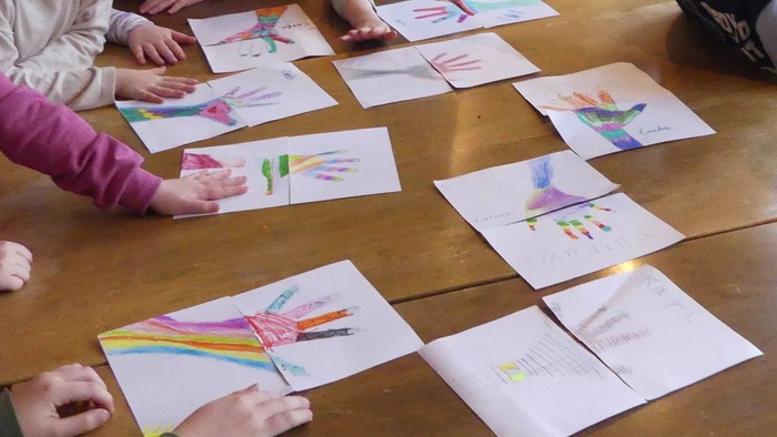 Kinder versammeln sich um einen Tisch, auf dem bunte Handabdruck-Kunst ausgestellt ist.