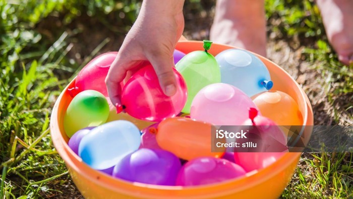 Eine Kinderhand greift in eine Schale mit bunten Wasserbomben auf dem Rasen.