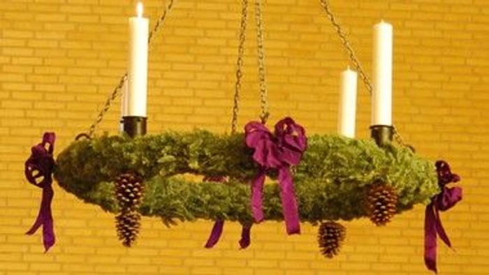 En julekrans med lysstake og fjøs og røde bænder hænger på en mur