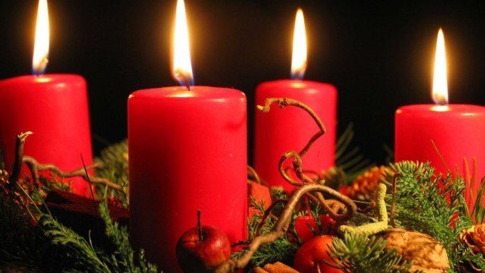 Fire røde lys på en adventskranse med grønne nåle og æble.