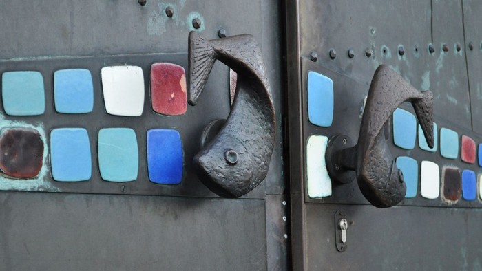 Antike Metalltür mit bunten Keramikfliesen in Fischform und rustikalen Eisengriffen.