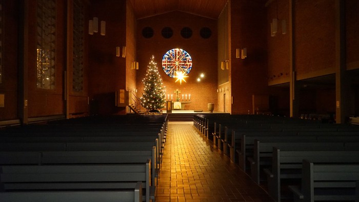 Warm beleuchteter Kirchengang, der zu einem geschmückten Weihnachtsbaum und einem erleuchteten Rundfenster führt.