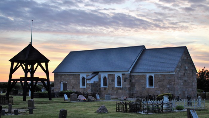 Hyggelig stenkirke med klokketårn i en fredfyldt, solbeskinnet kirkegård ved tusmørke.