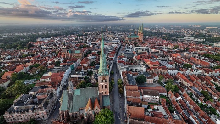 Luftaufnahme einer historischen europäischen Stadt mit einem markanten Kathedralturm und Gebäuden mit roten Dächern.