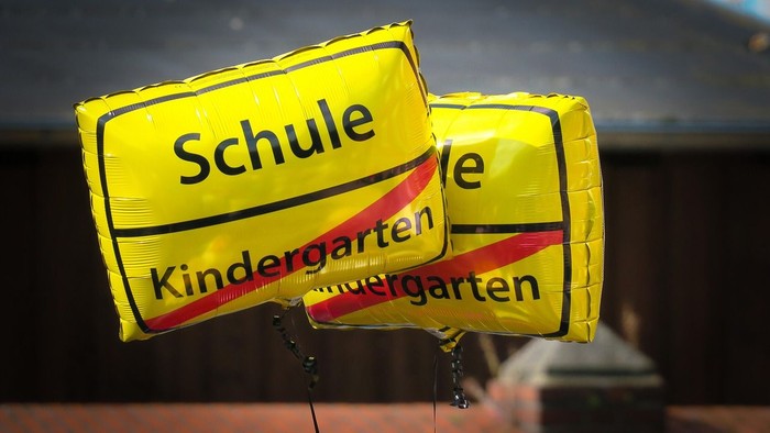 Zwei gelbe Luftballons mit den Aufschriften *„Schule“* und *„Kindergarten“* sind gut sichtbar ausgestellt.