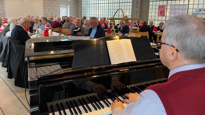 En livlig sammenkomst med en pianist, der spiller i en rummelig sal fyldt med siddende gæster.