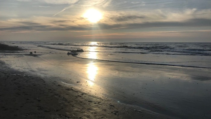 En solopgang over stranden med spåne og skyer i himlen