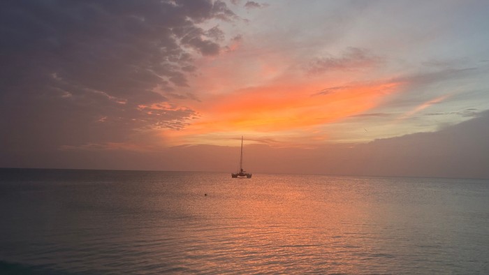 Das Foto zeigt einen Sonnenuntergang am Meer mit einem Boot im Hintergrund, der Himmel leuchtet orange