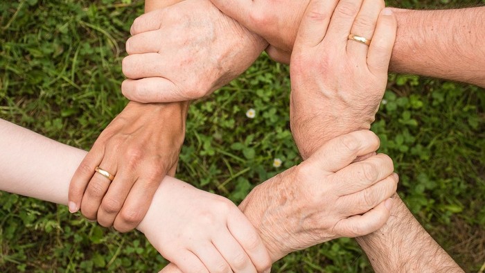 Eine Gruppe von Menschen, die sich im Freien im Kreis die Hände reichen und Einheit und Teamarbeit symbolisieren.