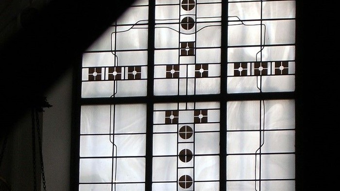 Komplexes Buntglasfenster mit geometrischen Mustern und Kreuzen in einer kathedralenartigen Umgebung.