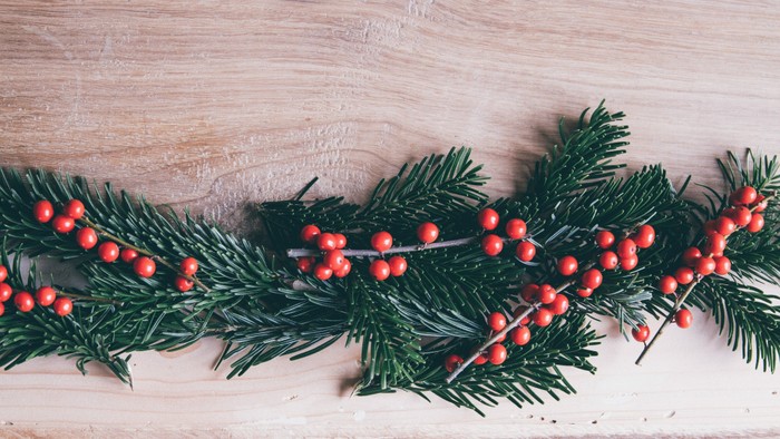 Ein Weihnachtsdekoration aus Tannenzweigen und Beeren liegt auf einem Holztisch.