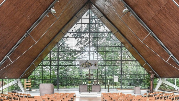 Moderne Kircheninnenraum mit hölzernen Sitzreihen, hohen Glaswänden und einem markanten Fisch-Motiv aus Buntglas.