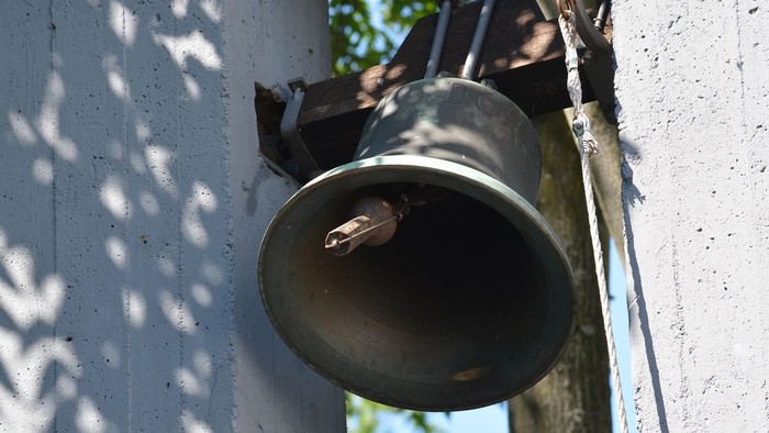 Eine Glocke ist an der weißen Wand befestigt.