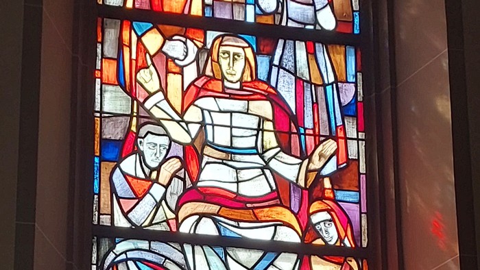 Buntglasfenster mit biblischen Szenen in leuchtenden Farben und religiösen Figuren in einer Kirche.