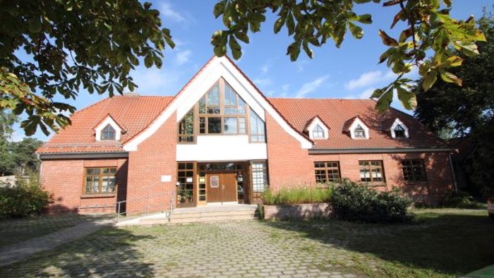 Bezauberndes Backsteingebäude mit zentralem Giebelportal und Kopfsteinpflasterhof, umgeben von Grünflächen.