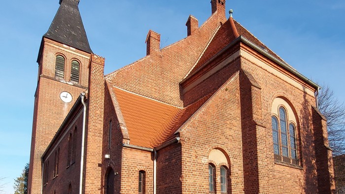 Kirchengebäude aus Ziegeln mit spitzem Turm und mehreren Fenstern
