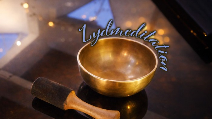En gylden syngeskål med en kølle hviler på en reflekterende overflade, mærket