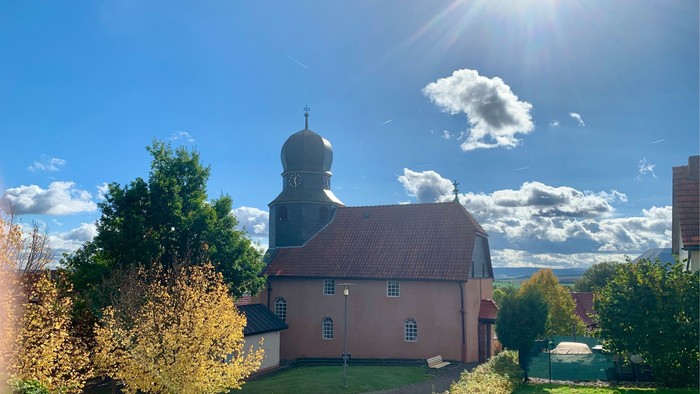 Sonnenbeschienene Kirche mit Kuppel in einem gepflegten, landschaftlich gestalteten Innenhof unter einem strahlend blauen Himmel.
