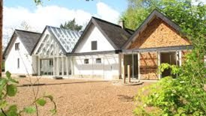 Moderne toetagers hus med skrå tage og åben terrasseområde omgivet af grønne områder.