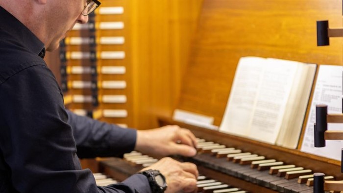 Eine Person, die an einer Orgel spielt und vor sich geöffnete Notenblätter hat.