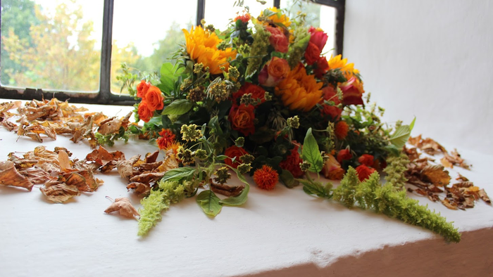 En blomsterarrangement med røde og gule blomster på en hvid flade ved et vindue
